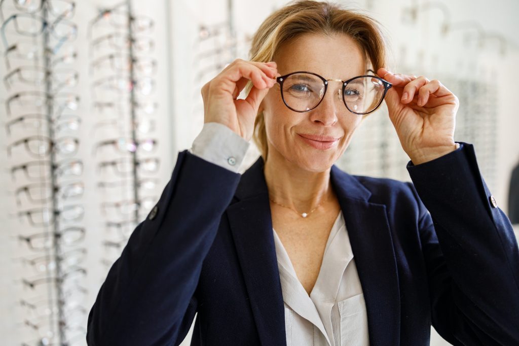 happy middle aged woman trying on stylish eyeglass frames at Oakville optometry clinic for dry eye care